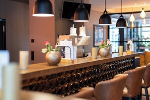 Un área de recepción de hotel moderna con un mostrador de madera, iluminación colgante y una planta decorativa.