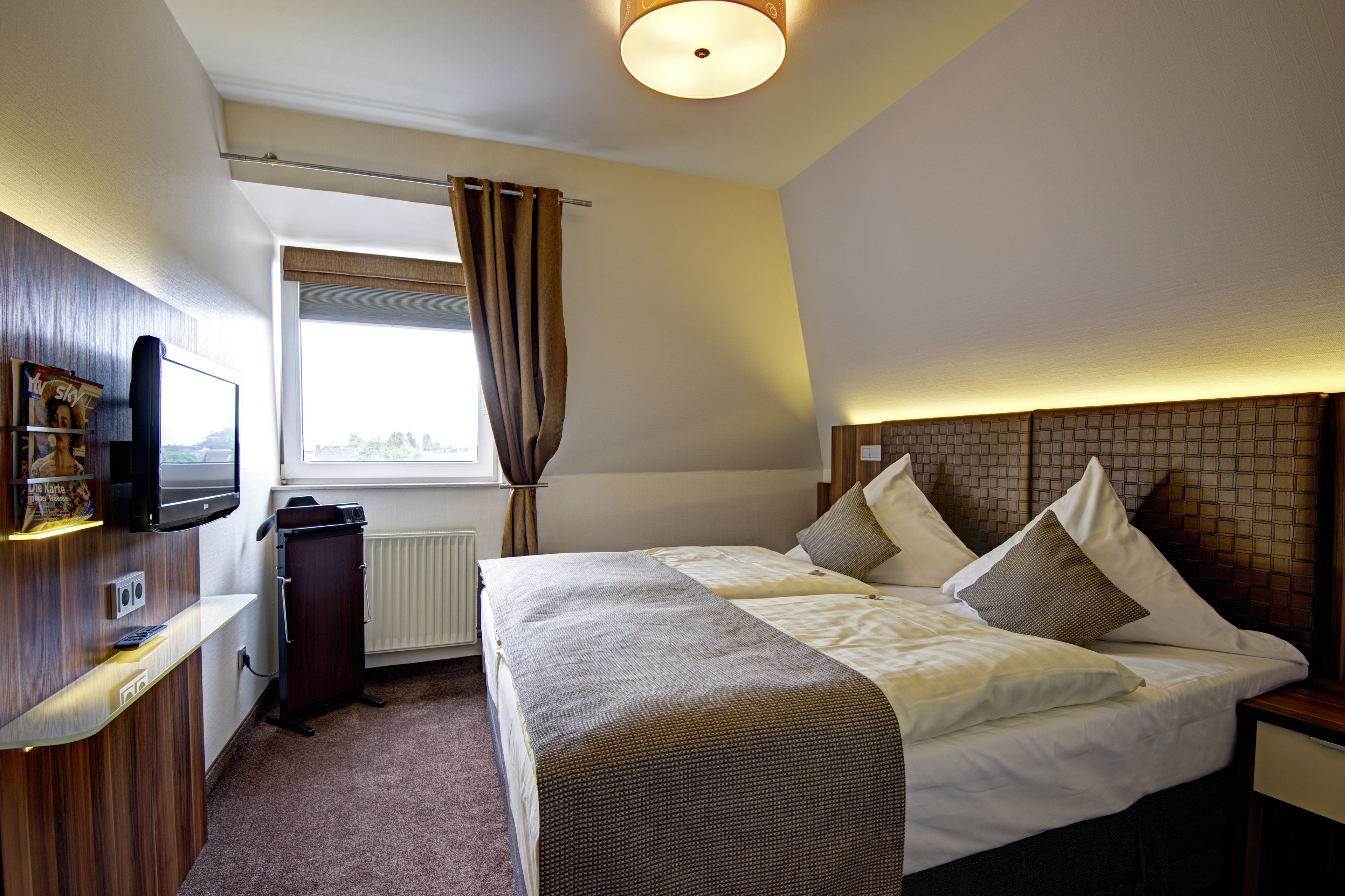 Ein Hotelzimmer mit Bett, Fernseher, Schreibtisch und einem Fenster mit Vorhängen.