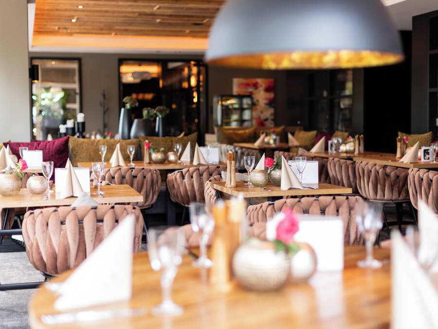 Um restaurante com mesas de madeira, cadeiras estofadas e um grande lustre.