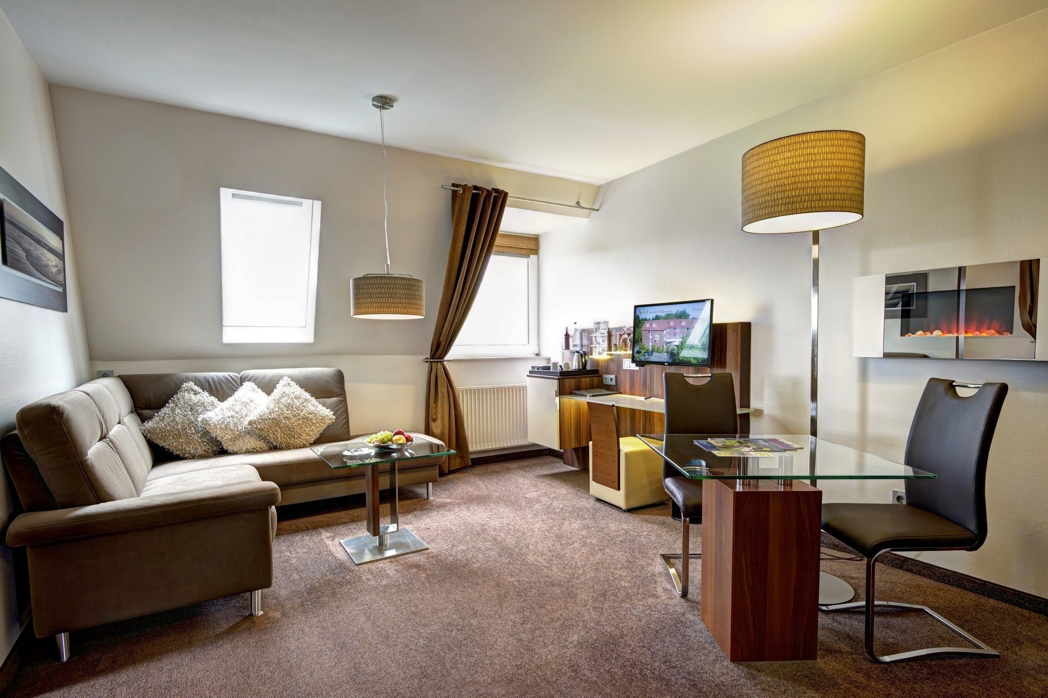 Ein modernes Hotelzimmer mit einer Couch, einem Glastisch, einem Schreibtisch mit Computer, einem Sessel und einem Fernseher.