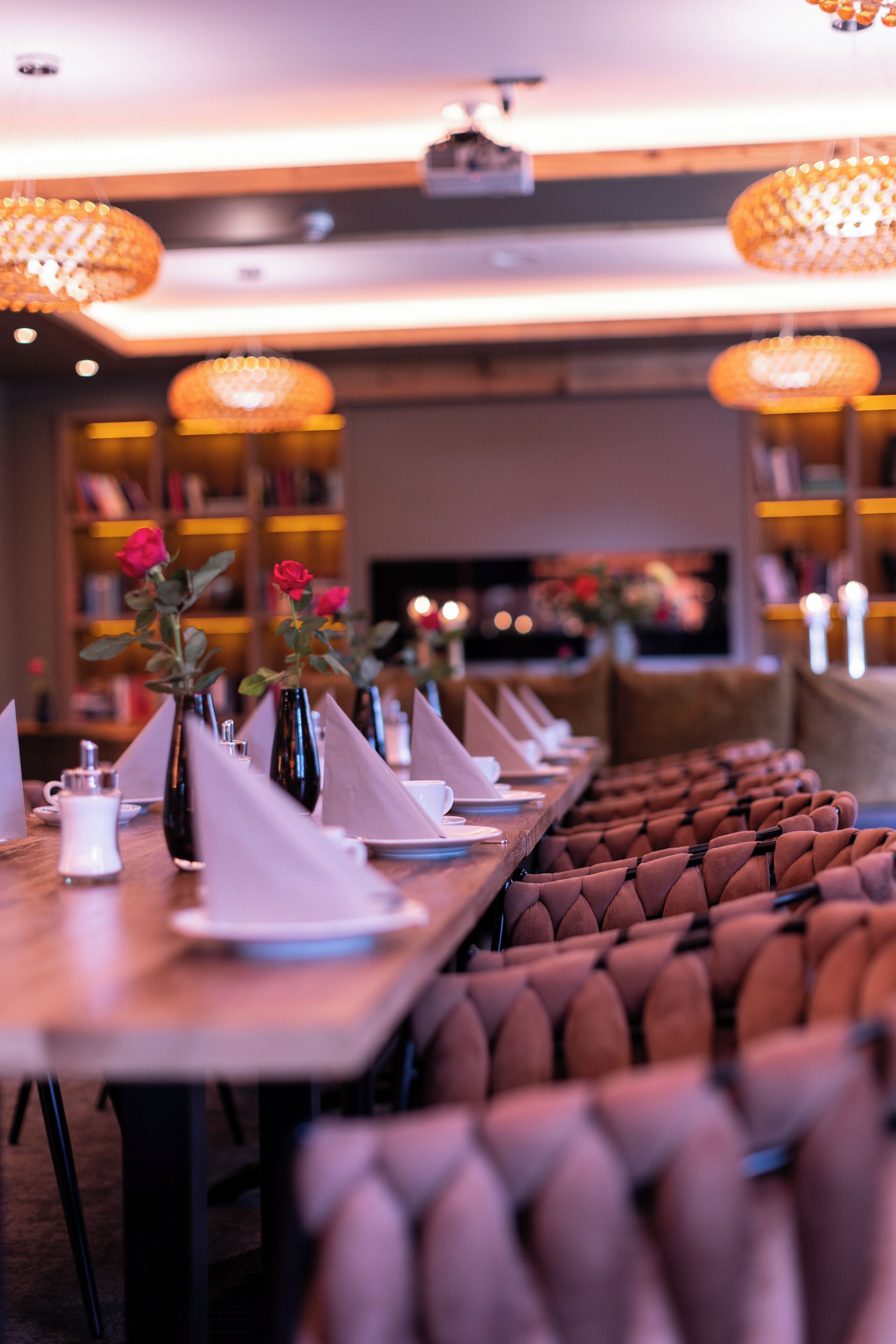 Comedor con una mesa larga dispuesta para varios comensales, jarrones con flores y una fila de sillas tapizadas.