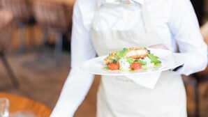Una persona con camisa y delantal blancos sostiene un plato de comida.
