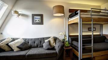 A room with a grey sofa, a bunk bed, a small table with a lamp, and a framed picture on the wall.