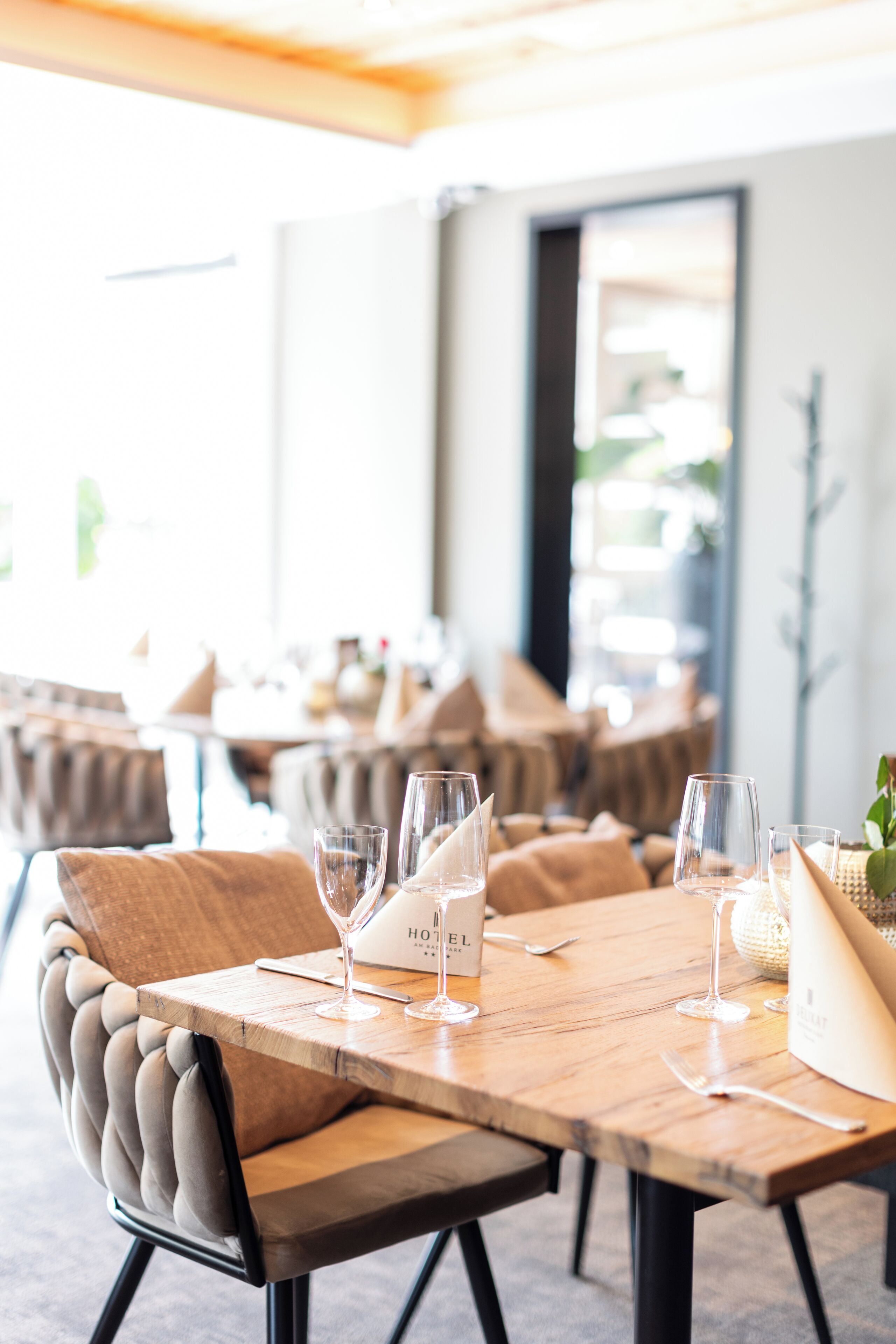 A dining area with a wooden table set for two, featuring a menu and wine glasses.
