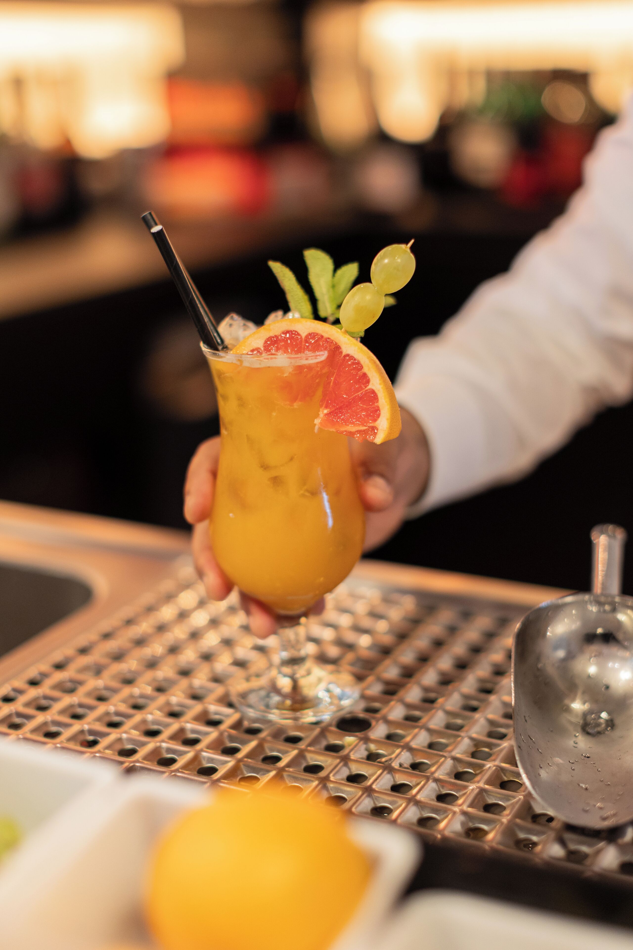 A cocktail with a straw and garnishes, held by a person.
