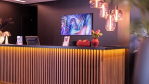 Una recepción de diseño moderno, con un televisor de pantalla plana, un jarrón rojo con flores y una zona de recepción elegante e iluminada.
