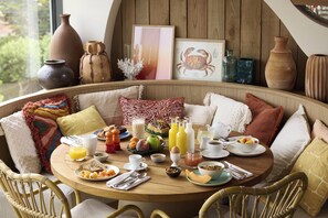 A round dining table with breakfast items, surrounded by wicker chairs, in a room with wooden walls and various decorative items.