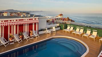 A rooftop pool with lounge chairs, a view of the ocean, and a distant mountain.