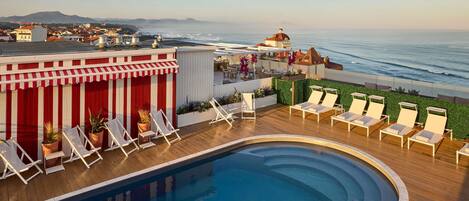 A rooftop pool with lounge chairs, a view of the ocean, and a distant mountain.