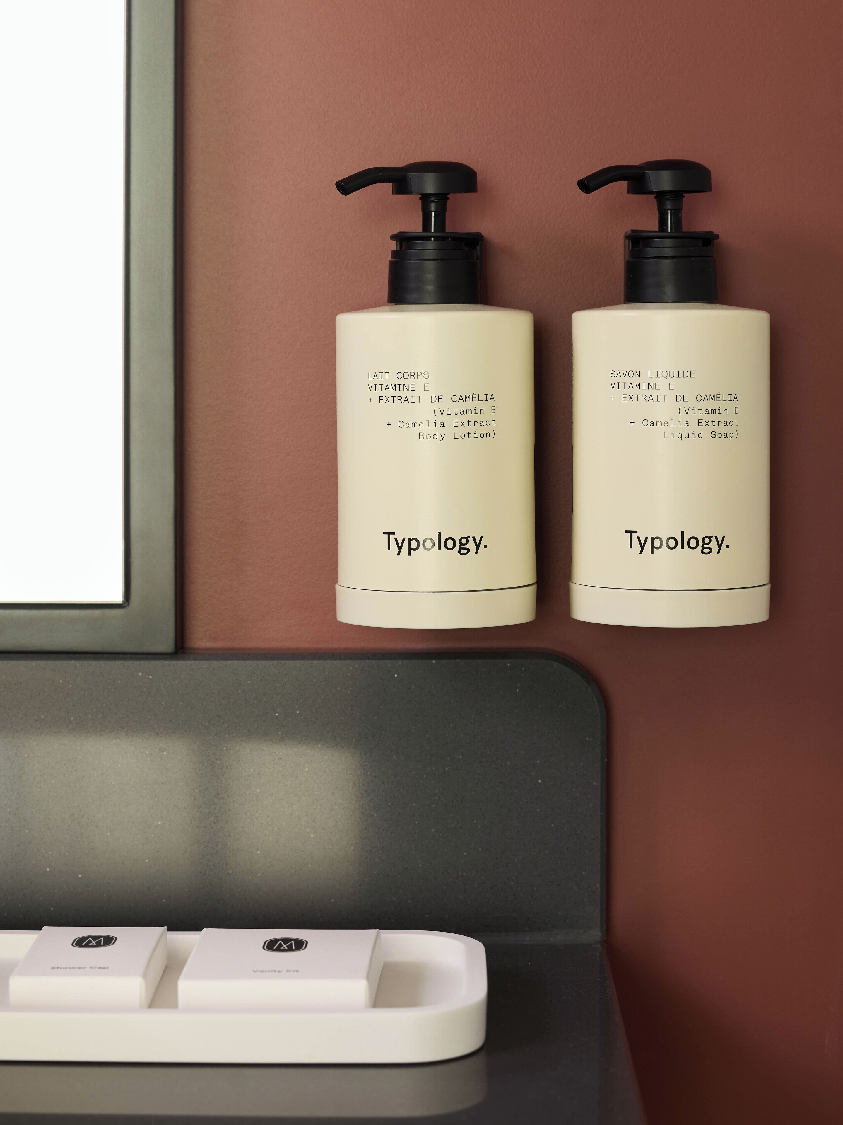 To flasker Typology bodylotion og flydende sæbe på en hylde.