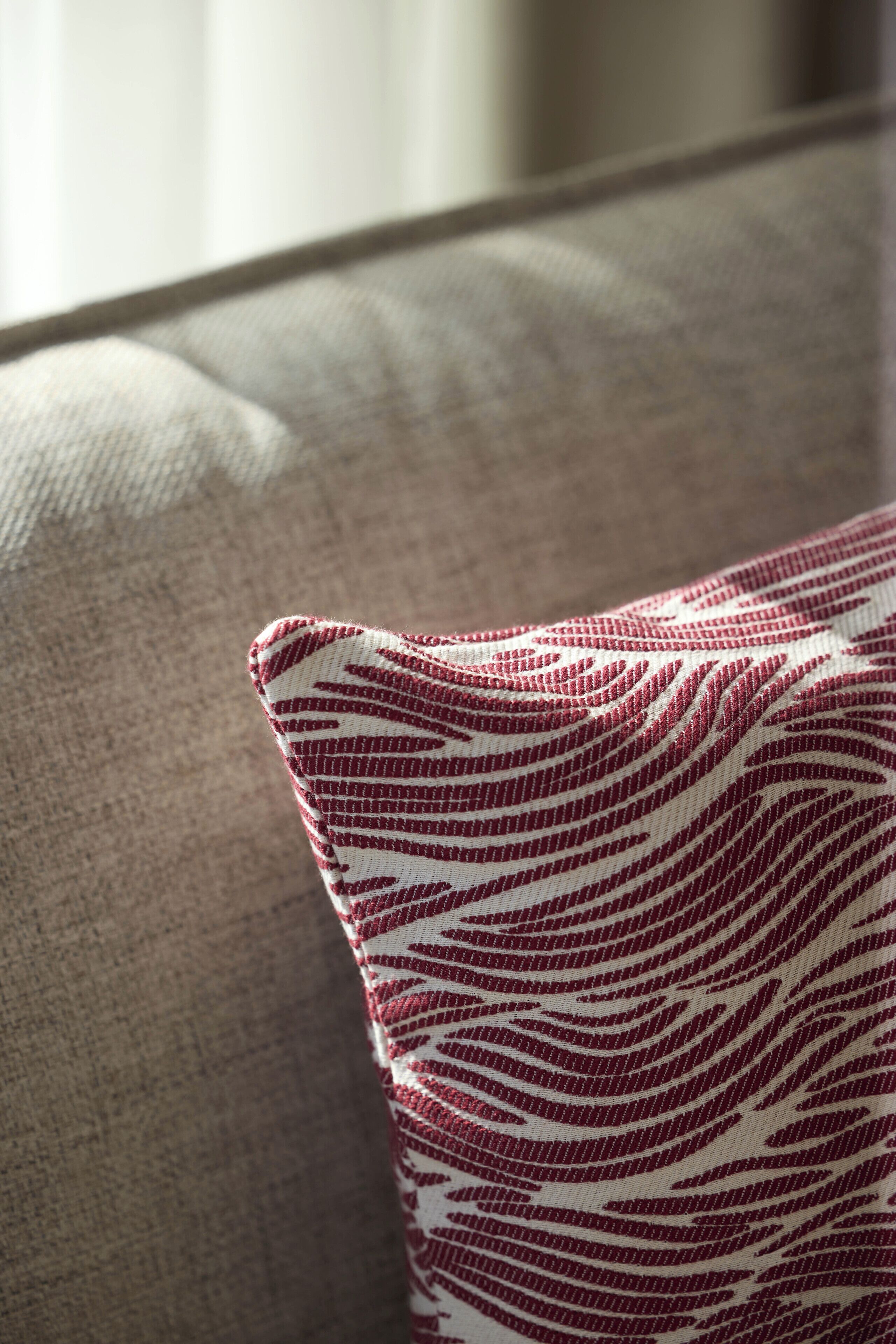 A close-up of a fabric with a red and white pattern on a beige couch.