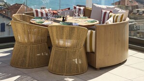 A round table with wicker chairs and cushions, set on a balcony with a view of the sea and distant mountains. - Le Talaia Hôtel & Spa Biarritz - MGallery Collection (Biarritz)