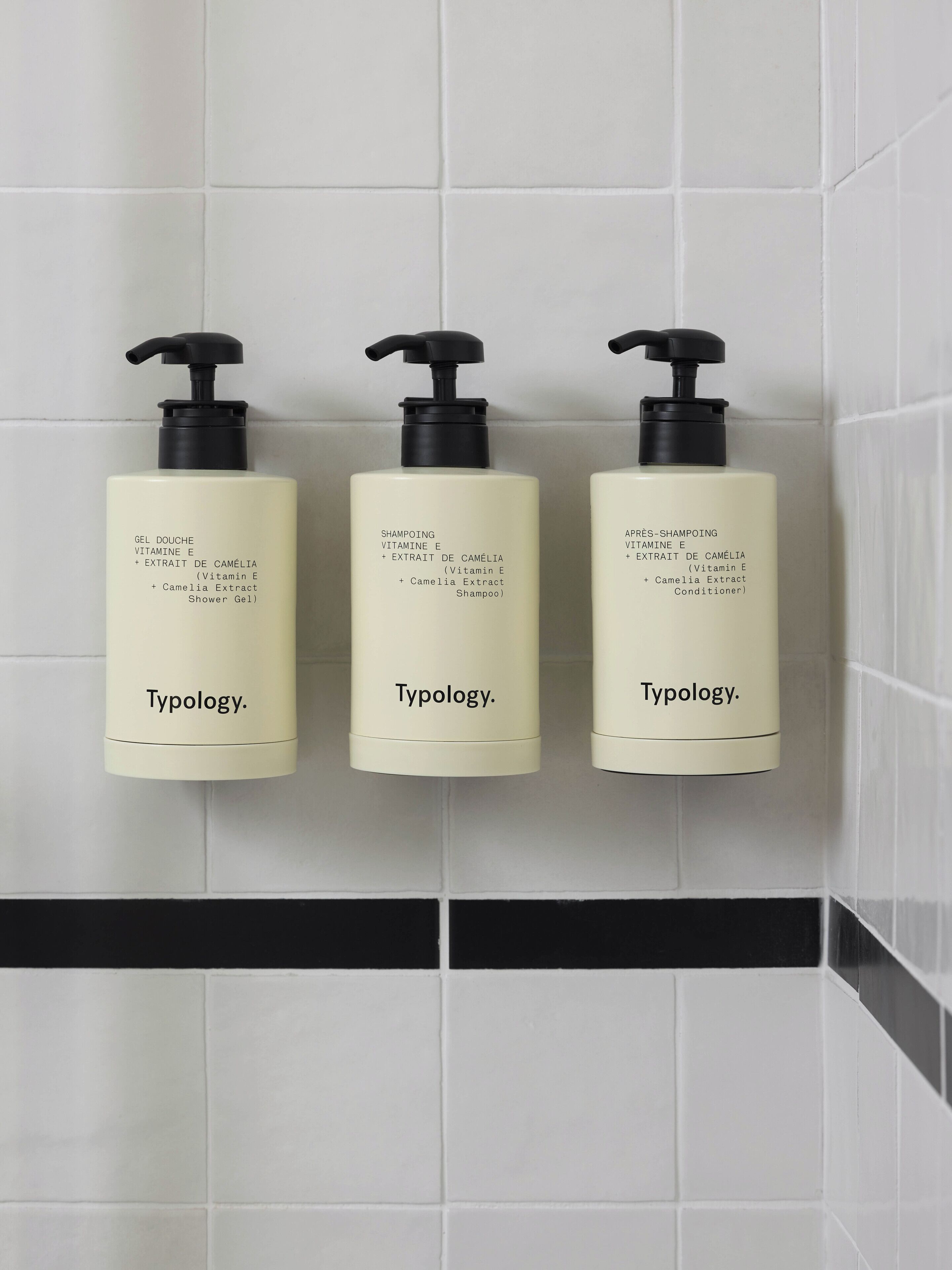 Tres botellas de productos de cuidado de la piel Typology sobre una pared de azulejos.