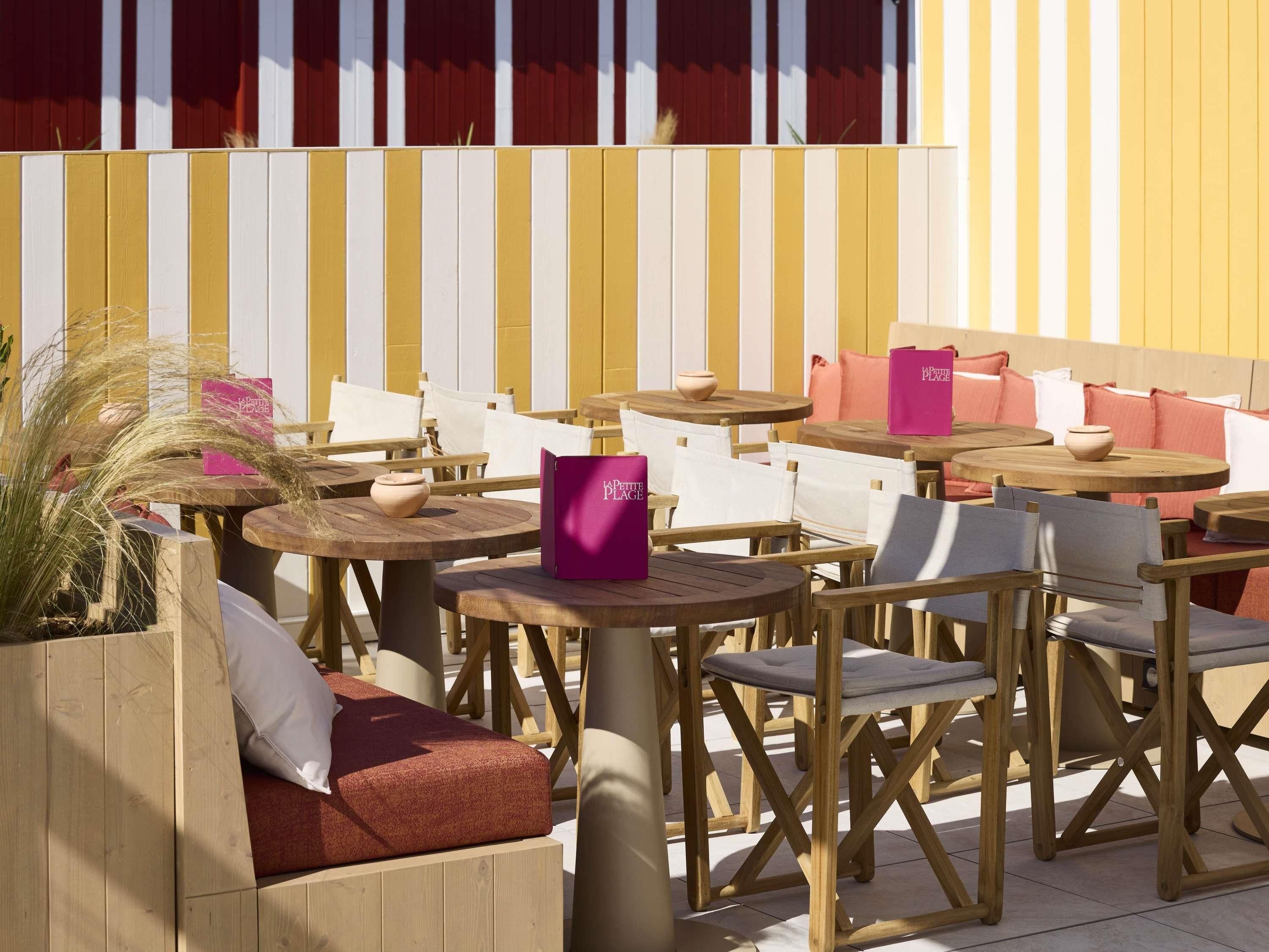 Un espace extérieur aménagé avec des tables et des chaises en bois, un sac rose et un coussin rouge.