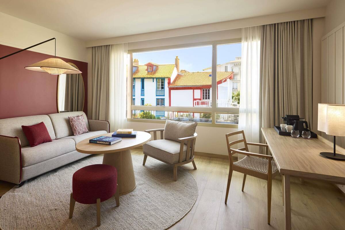 Habitación de hotel con sofá, sillón, mesa de centro y mesa de comedor con lámpara.