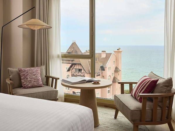 A hotel room with a large window, a bed, two armchairs, a small round table, and a floor lamp. - Le Talaia Hôtel & Spa Biarritz - MGallery Collection (Biarritz)