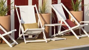 Twee witte lounge stoelen met kussens, geplaatst bij een zwembad met een rood-wit gestreept hek op de achtergrond.