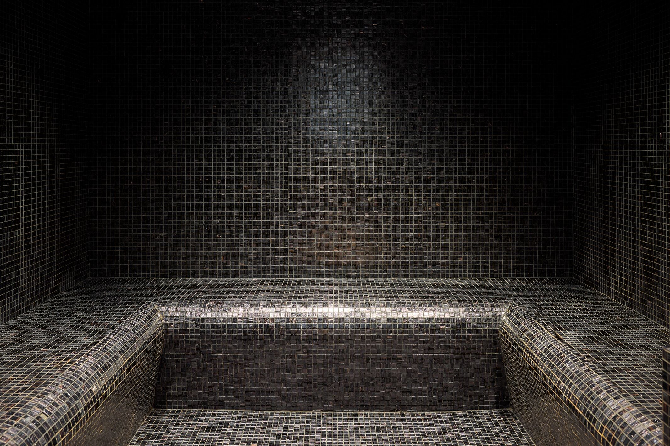 Un baño con baldosas, zona de ducha rectangular y un lavamanos pequeño.