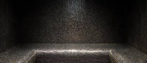 A tiled bathroom with a rectangular shower area and a small sink.