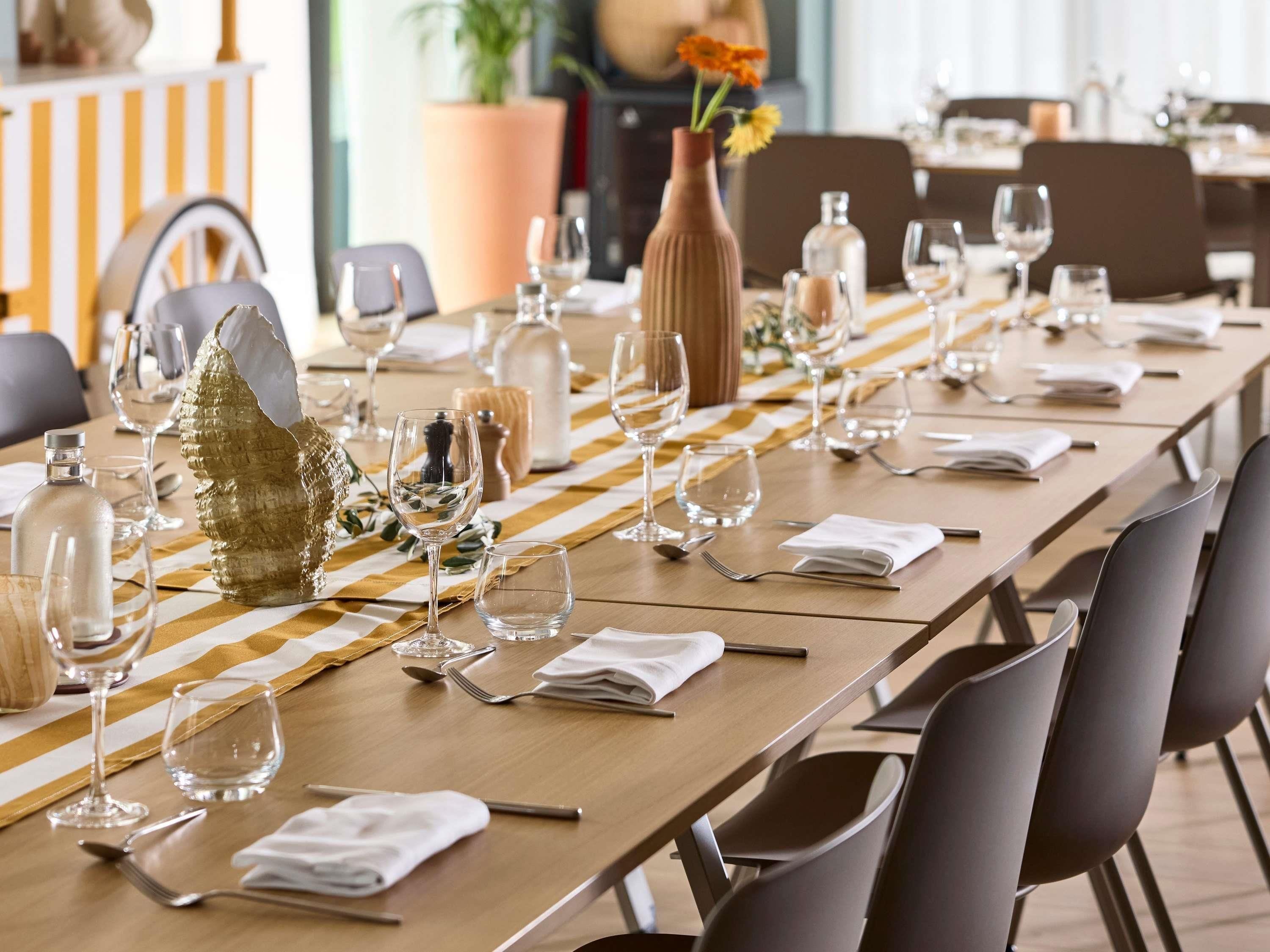 Una larga mesa de comedor dispuesta con sillas, copas y un florero con flores.