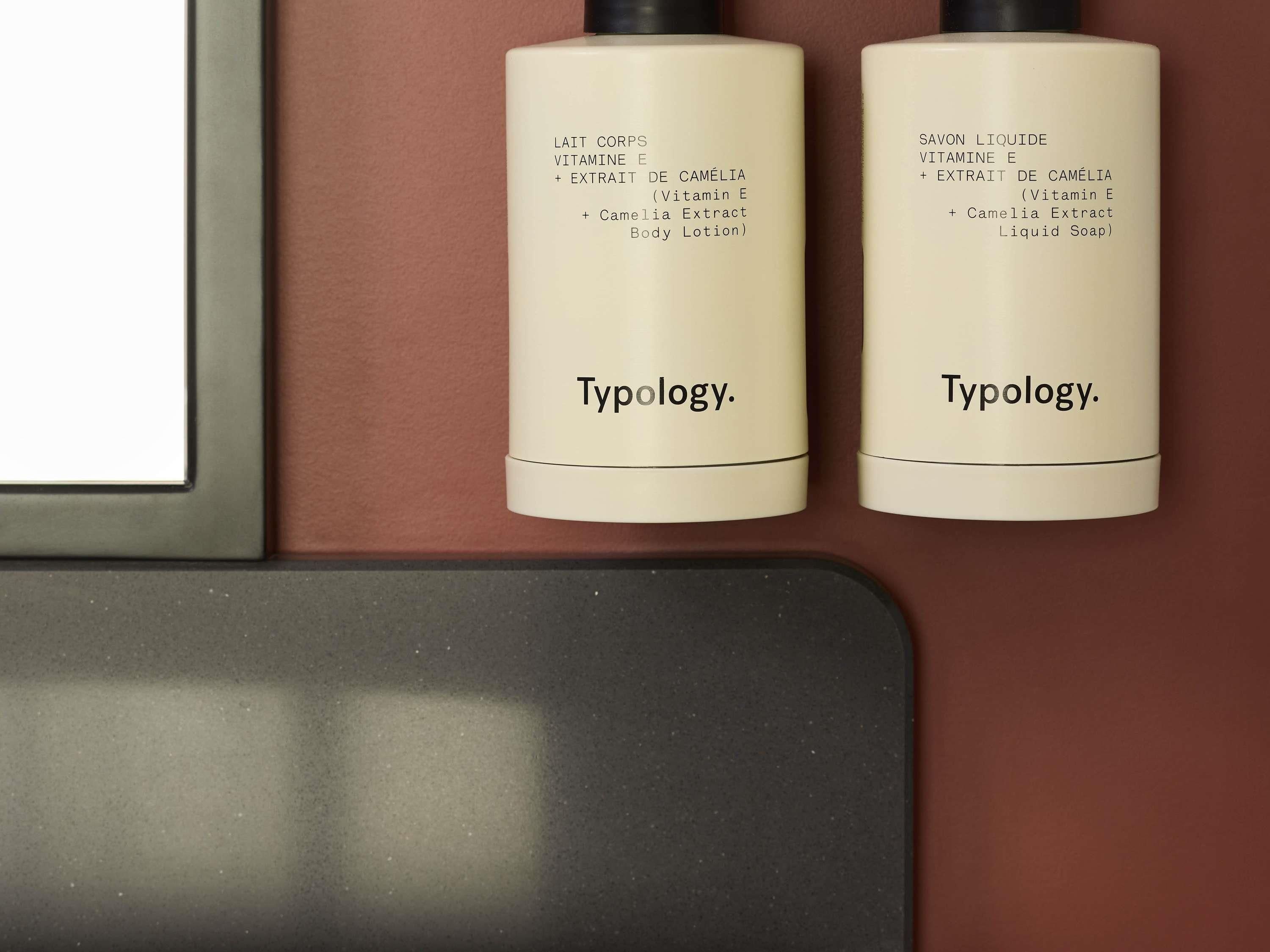 Dos botellas de loción corporal y jabón líquido Typology en una estantería.