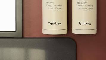 Dos botellas de loción corporal y jabón líquido Typology en una estantería.