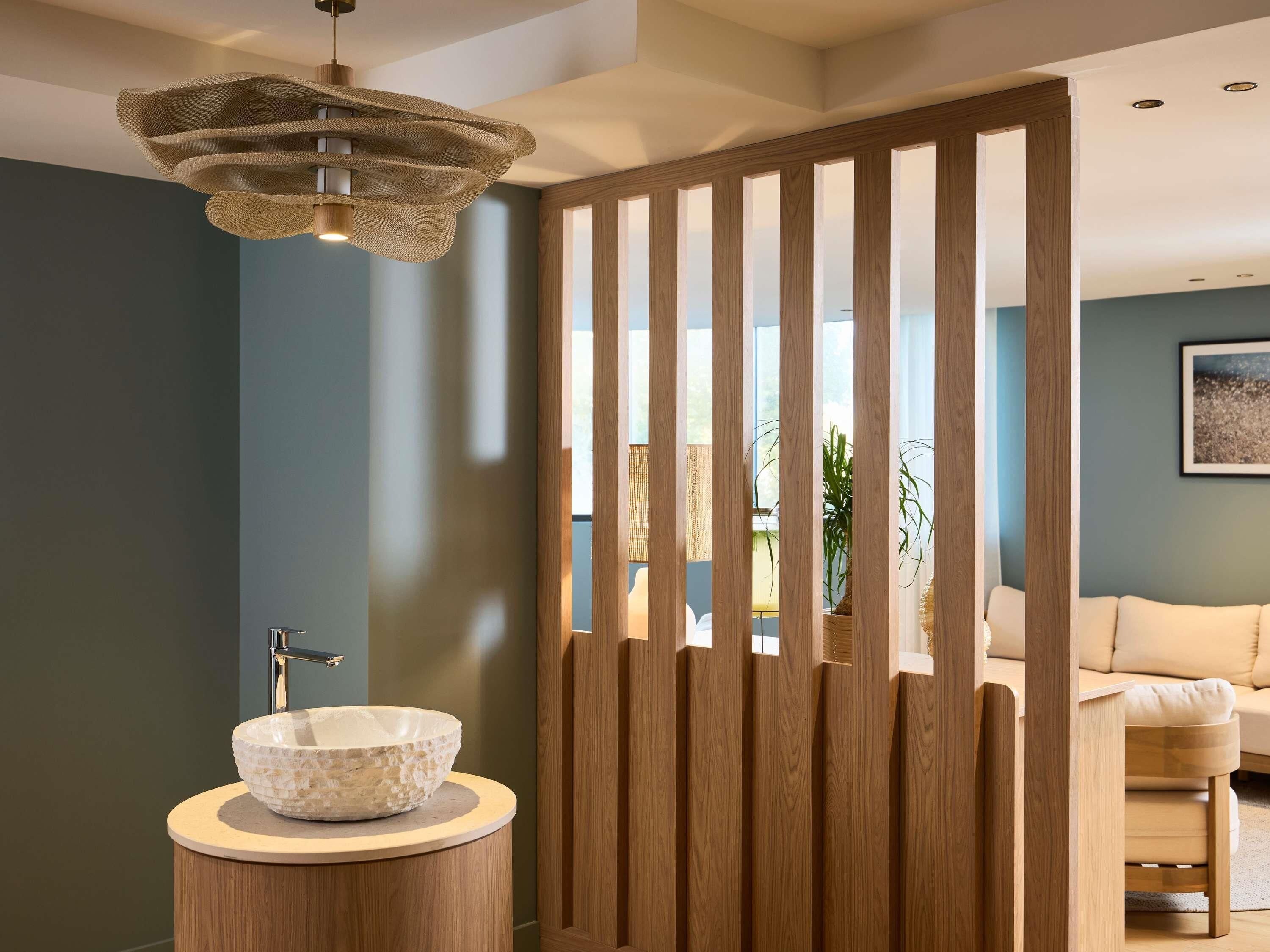 A modern bathroom with a stone sink, wooden panel divider, and a ceiling light fixture.