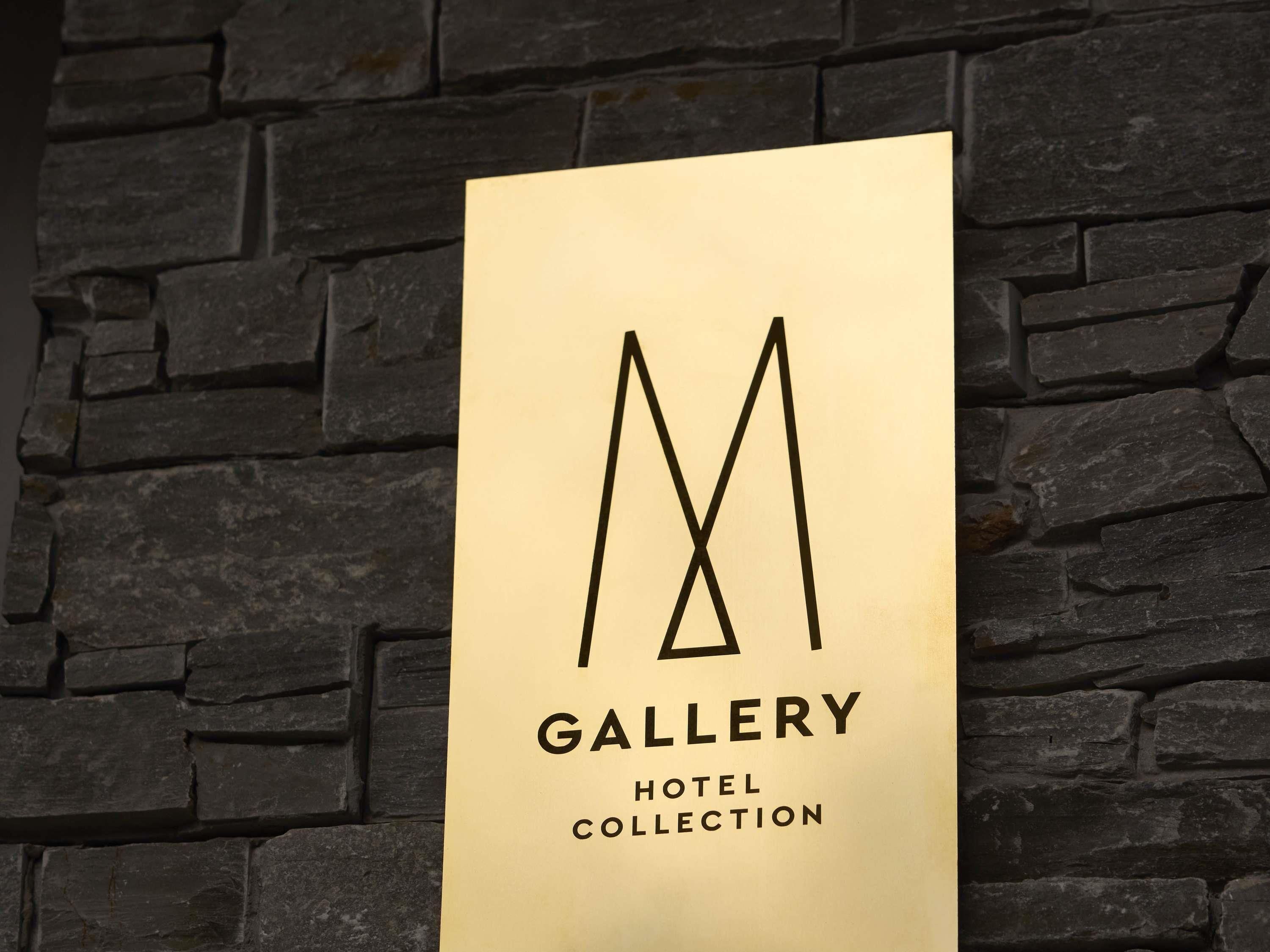 A sign with the text 'GALLERY HOTEL COLLECTION' against a stone wall background.