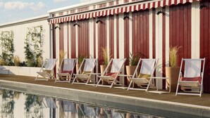 A poolside area with white lounge chairs and potted plants against a striped wall. - Le Talaia Hôtel & Spa Biarritz - MGallery Collection (Biarritz)