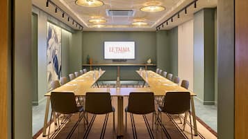 Et mødelokale med et langt bord, stole, et projektorskærm og et dekorativt loft.