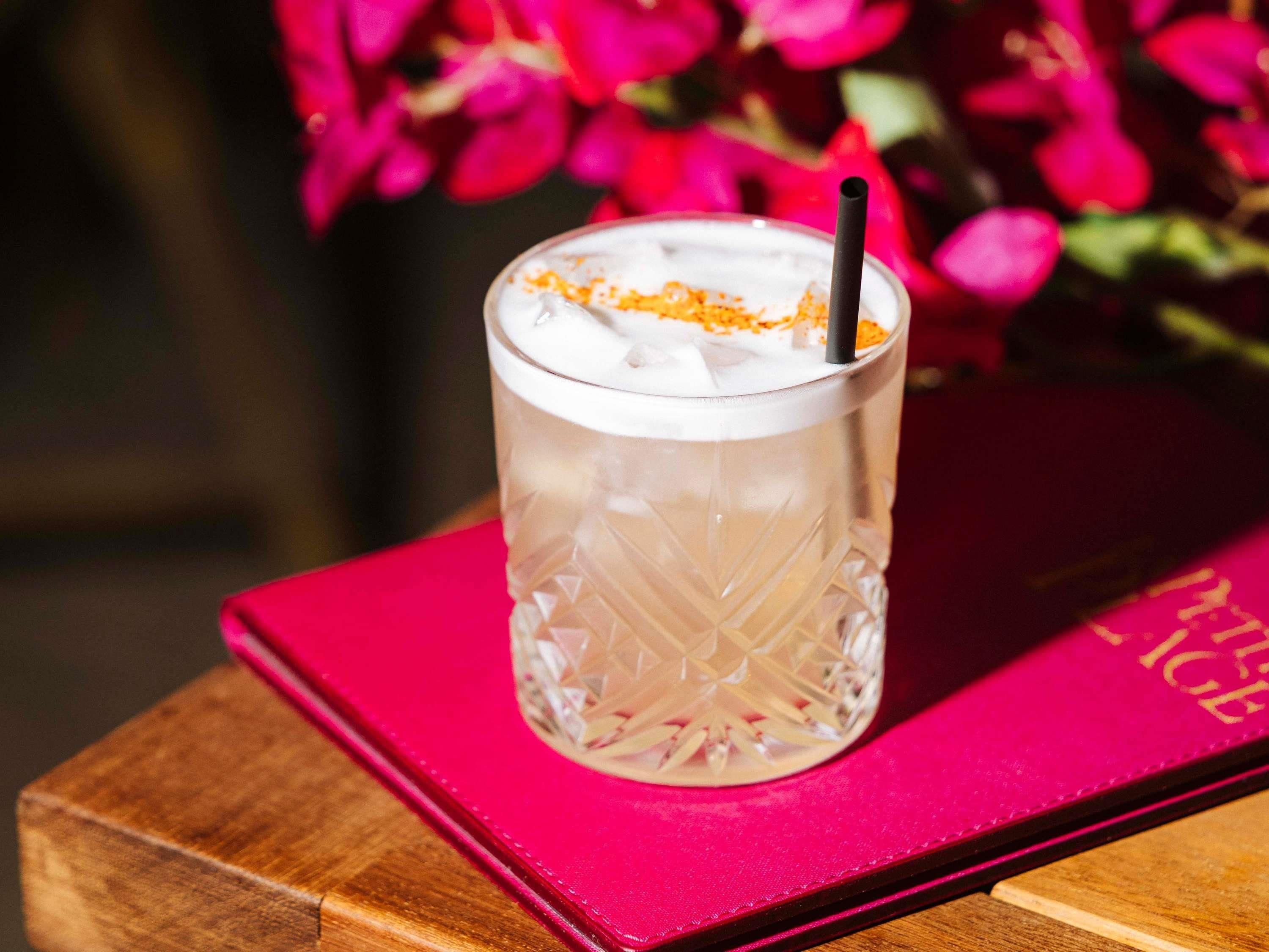 Un vaso transparente con una pajita, sobre una superficie de madera con un libro rosa a un lado.