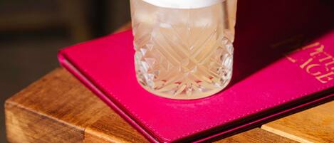 Un vaso transparente con una pajita, sobre una superficie de madera con un libro rosa a un lado.