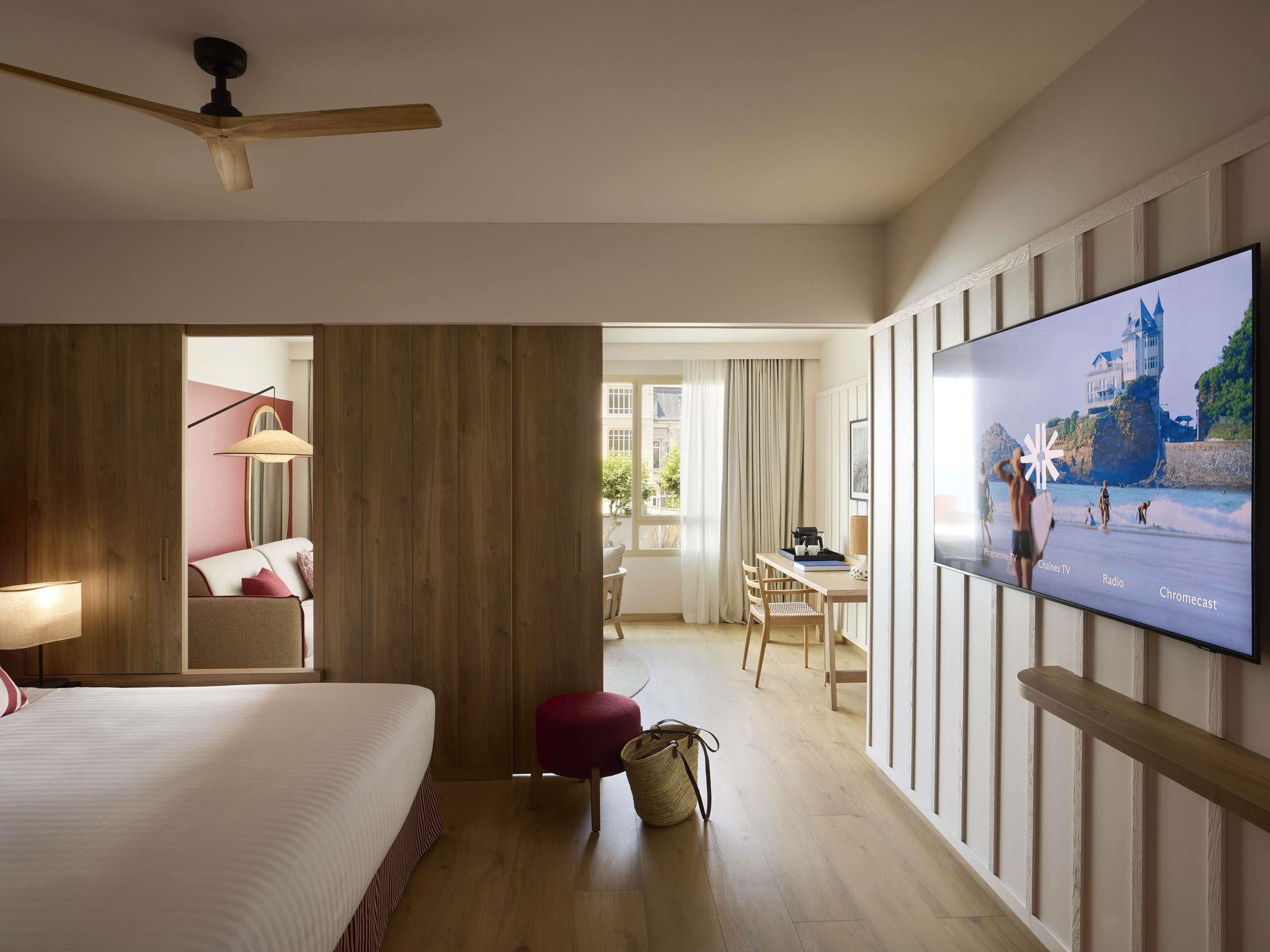 Habitación de hotel con cama, escritorio, televisión y vista a la playa.