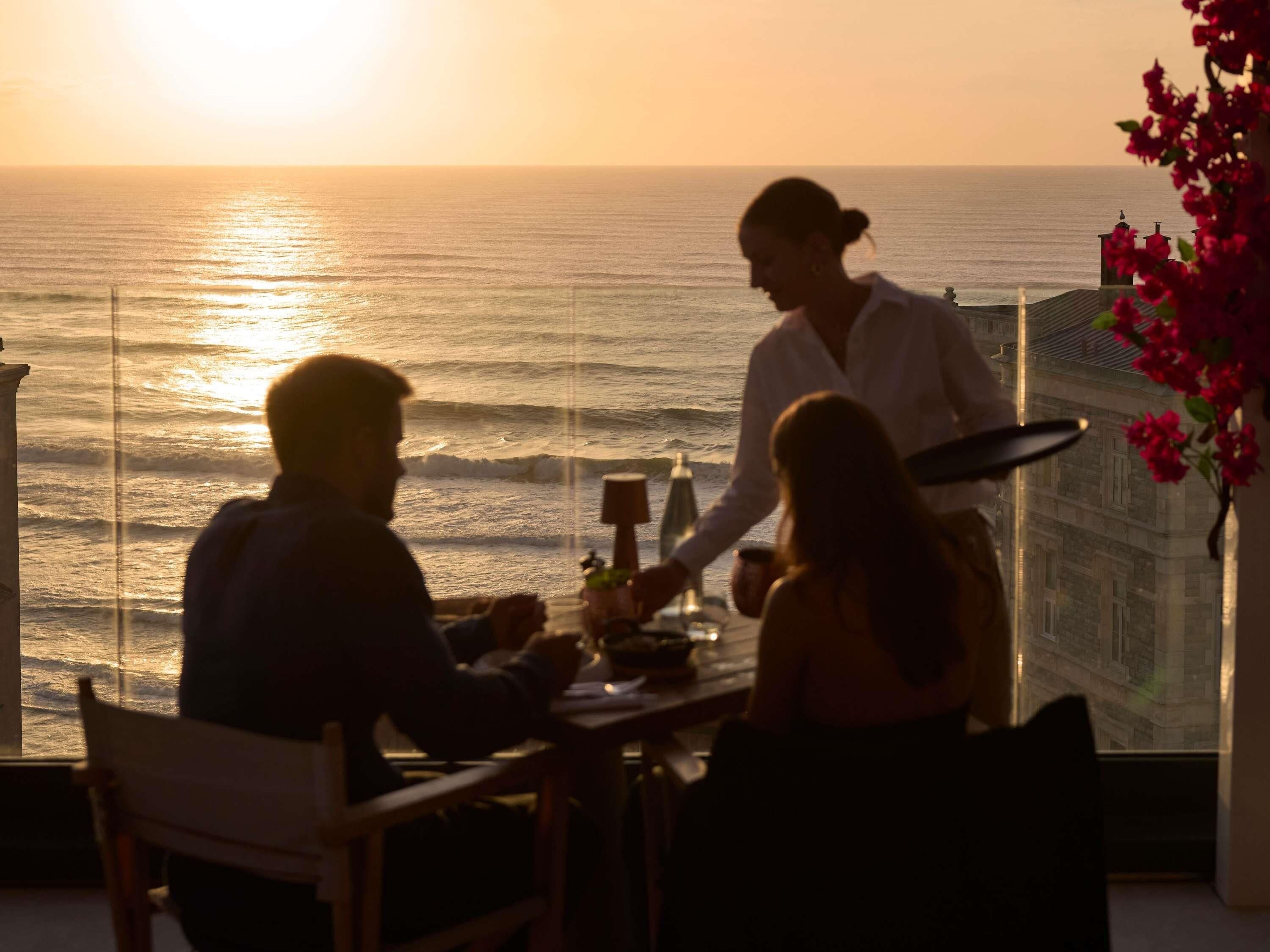 Zonsondergang vanaf een balkon met een tafel en stoelen, met uitzicht op de zee.