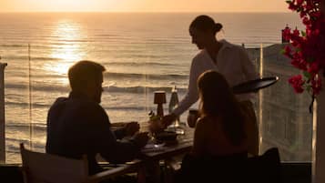 Vista al atardecer desde un balcón con mesa y sillas, con vista al mar.