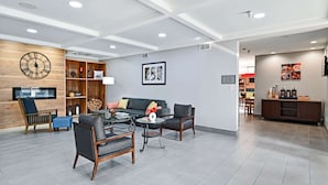 A modern living room with a sofa, chairs, and a coffee table. There is a wooden shelf with decorative items and a clock on the wall.