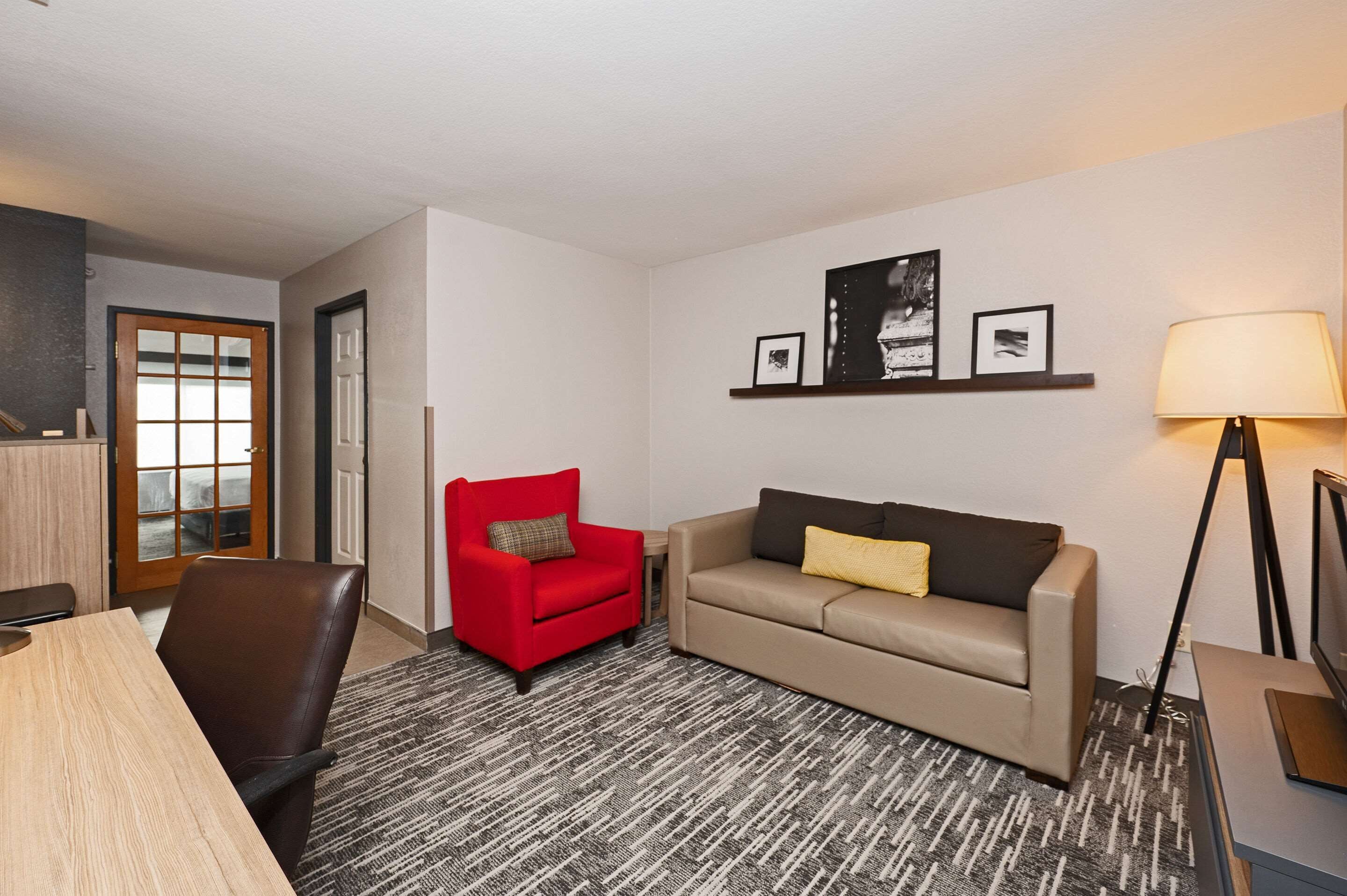 Habitación de hotel con un sillón rojo, sofá color beige y una lámpara.