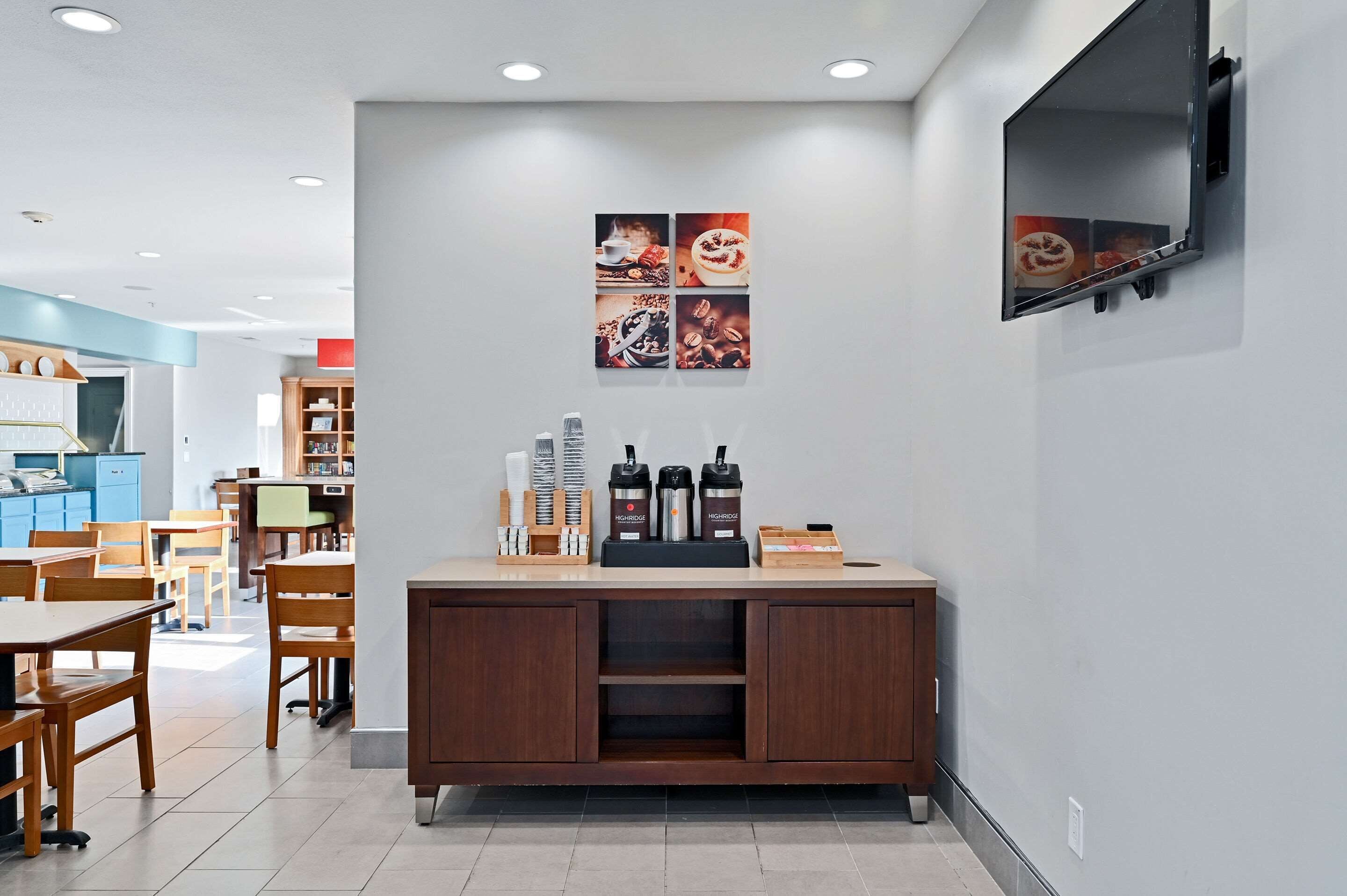 A modern cafe with wooden furniture, a coffee station, and a wall-mounted TV.