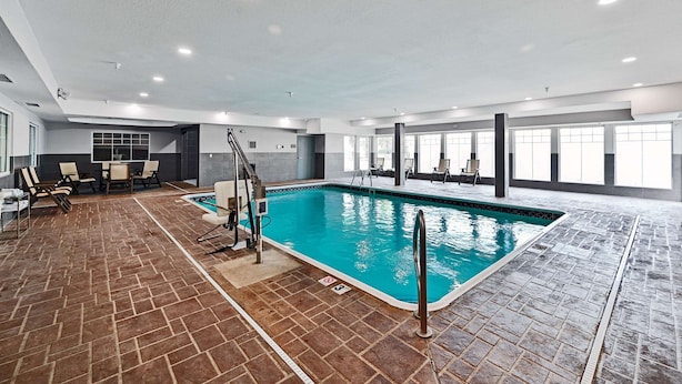 An indoor swimming pool with a tiled floor, a pool ladder, and a seating area with chairs and tables.