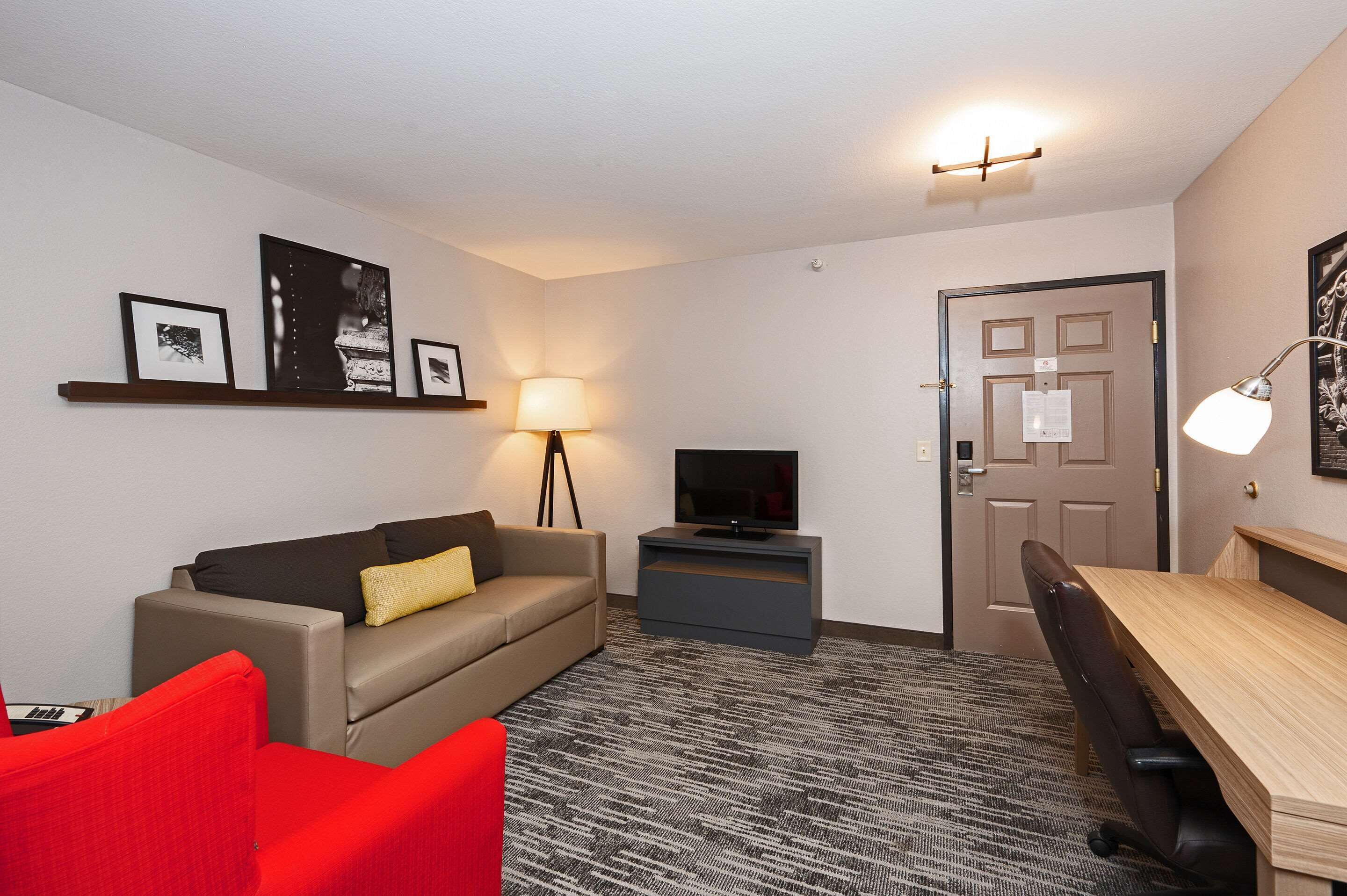 A hotel room with a sofa, a red chair, a TV on a stand, a desk, and a patterned carpet.
