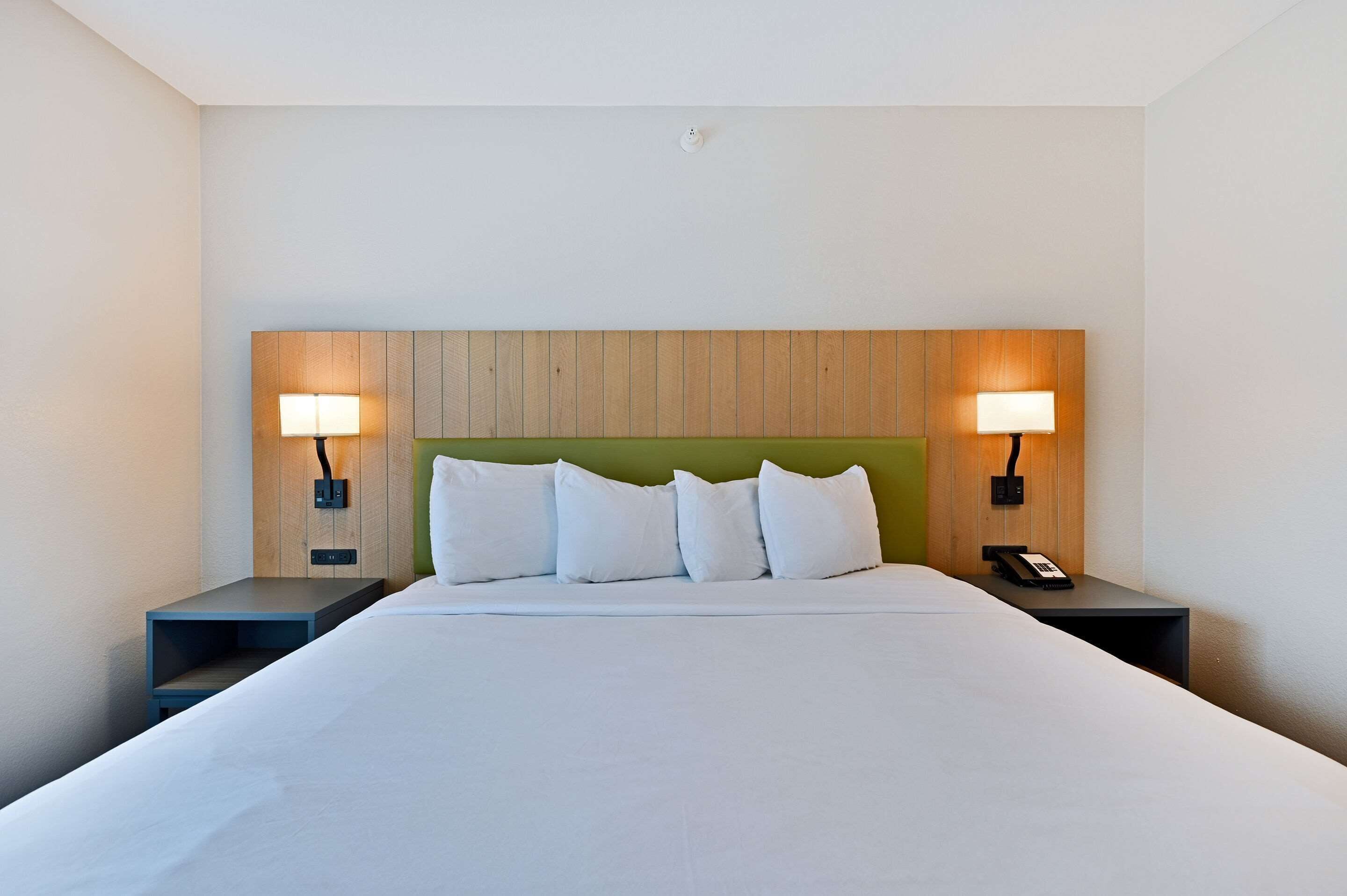 A hotel room with a large bed, two bedside tables with lamps, a green headboard, and a telephone on one of the tables.