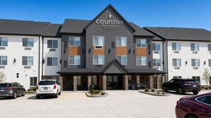 A Country Inn & Suites building with a modern design, featuring a prominent entrance and a parking area with several cars.