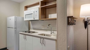 A compact kitchen with a refrigerator, microwave, sink, and wooden shelves above the countertop. - Extended Stay America Premier Suites Miami Coral Gables (Miami)