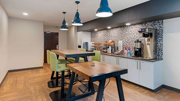 A modern kitchen with a coffee machine, a microwave, and a variety of kitchen appliances. There are two wooden tables with chairs, and a countertop with a coffee station. - Extended Stay America Premier Suites Miami Coral Gables (Miami)