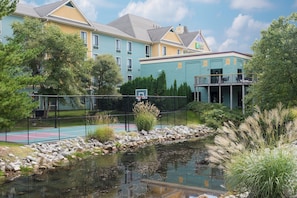 A hotel with a tennis court, a pond, and a building with a green facade.