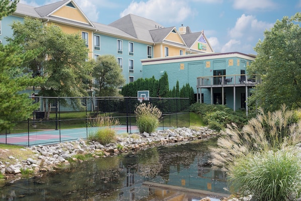 A hotel with a tennis court, a pond, and a building with a green facade.