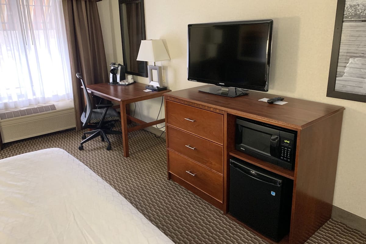 A hotel room with a bed, a desk with a computer, a television, a microwave, and a small refrigerator.