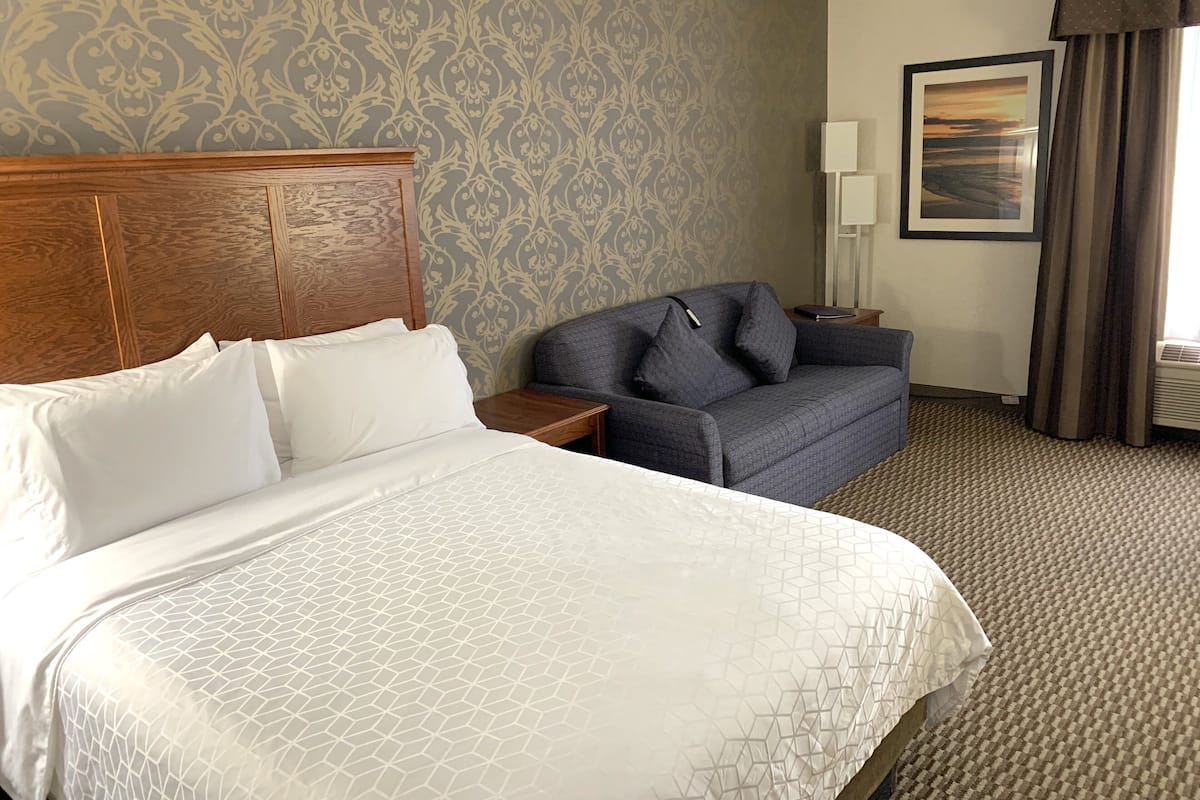A hotel room with a large bed, a sofa, a nightstand, a lamp, and a framed picture on the wall.