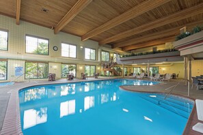 An indoor swimming pool with a wooden ceiling, multiple windows, and a staircase leading to an upper level.