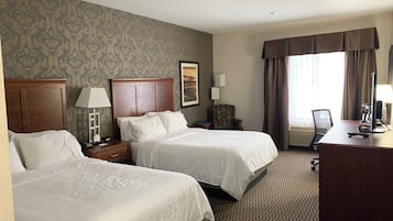 A hotel room with two beds, a desk, a chair, a lamp, a picture on the wall, and a window with curtains.